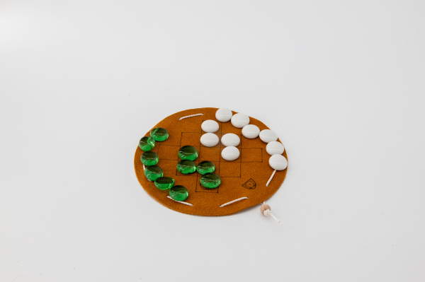 Queah, board game from Liberia on a round, light brown leather playing field with green and white playing pieces